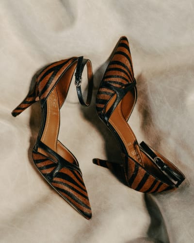 Pair of tiger print pointed toe heels displayed on a beige background.